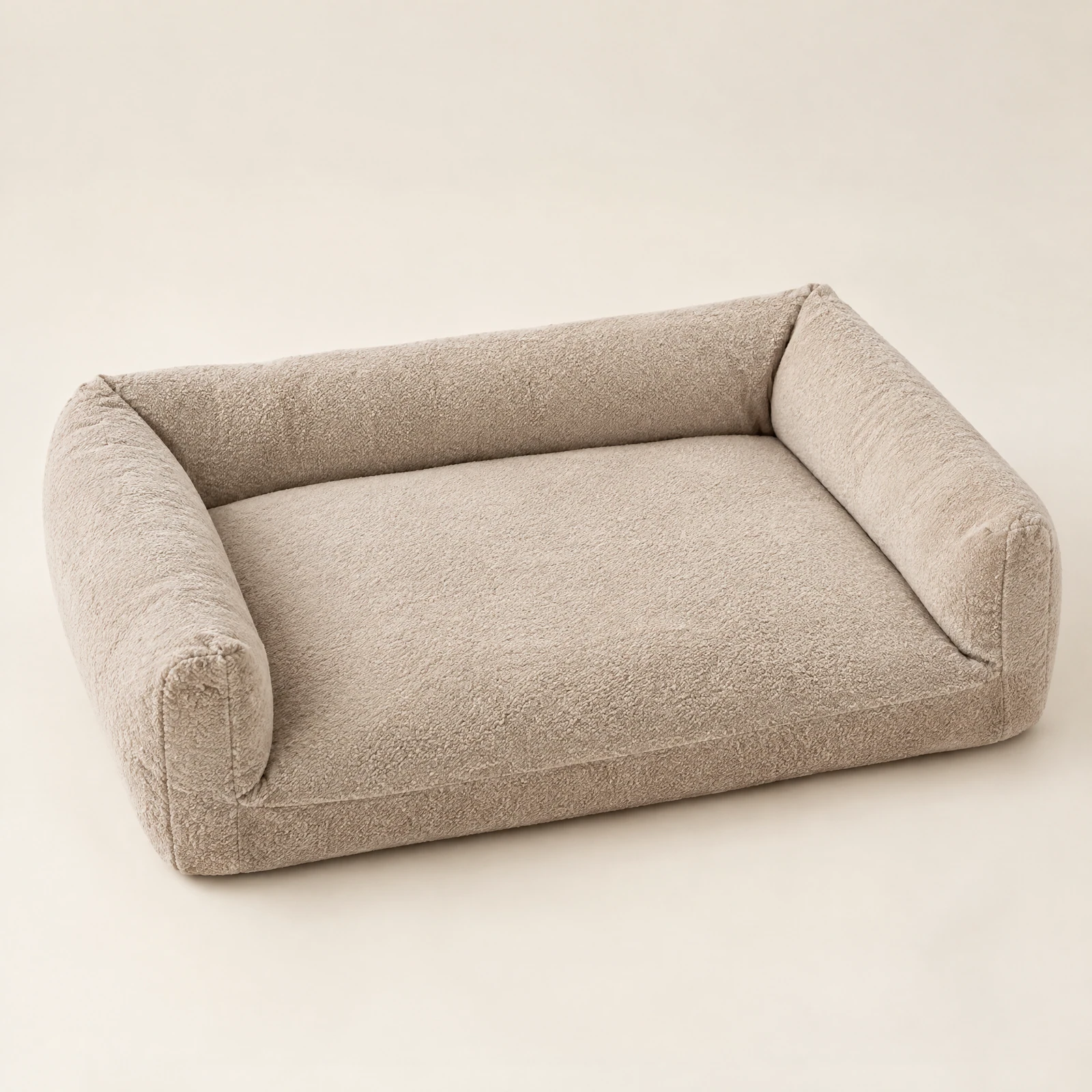 A rectangular oatmeal-colored textured dog bed with raised bolster sides on three edges, empty, on a cream background