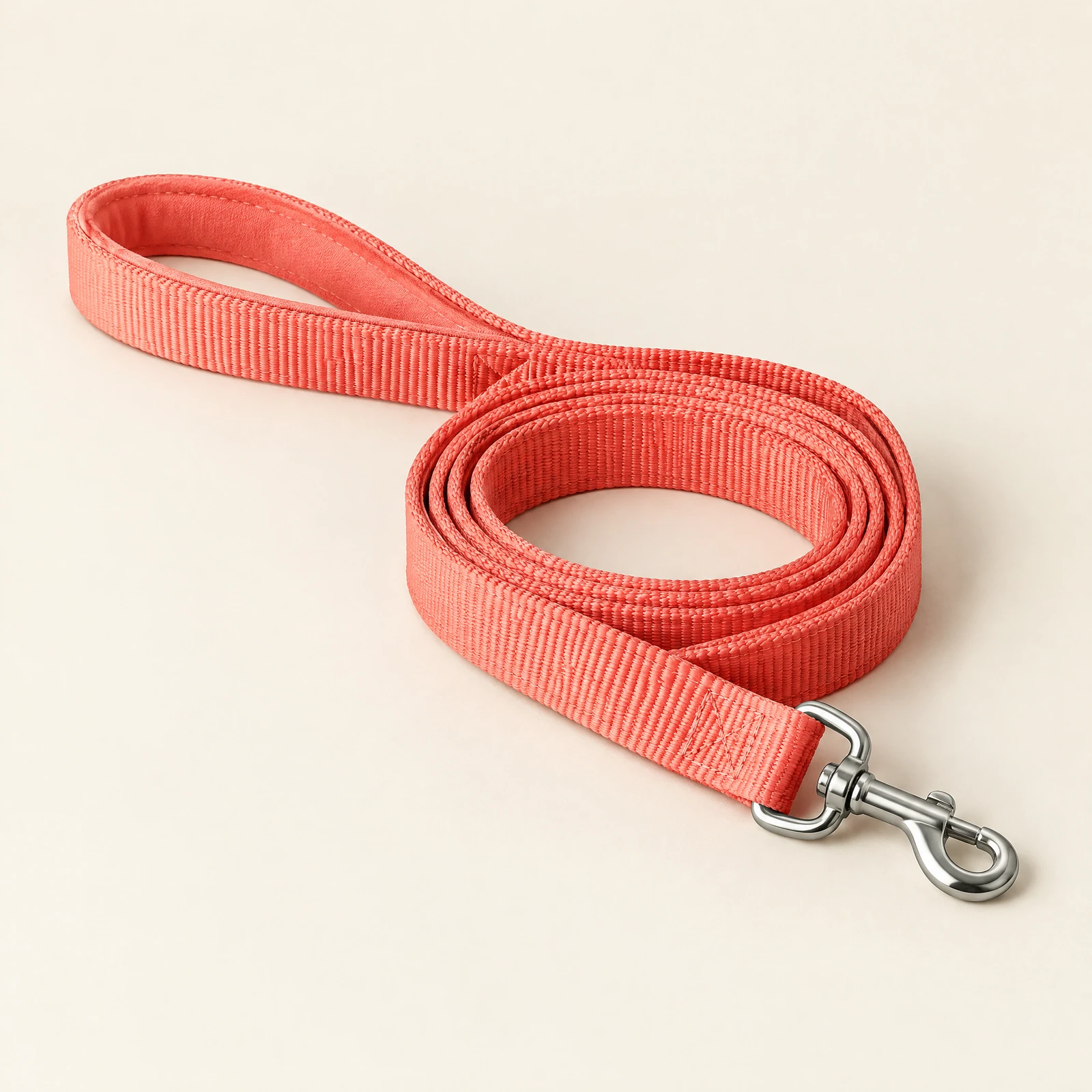 A coral dog leash with a padded loop handle and a swivel snap hook, laid in a loose coil on a cream background