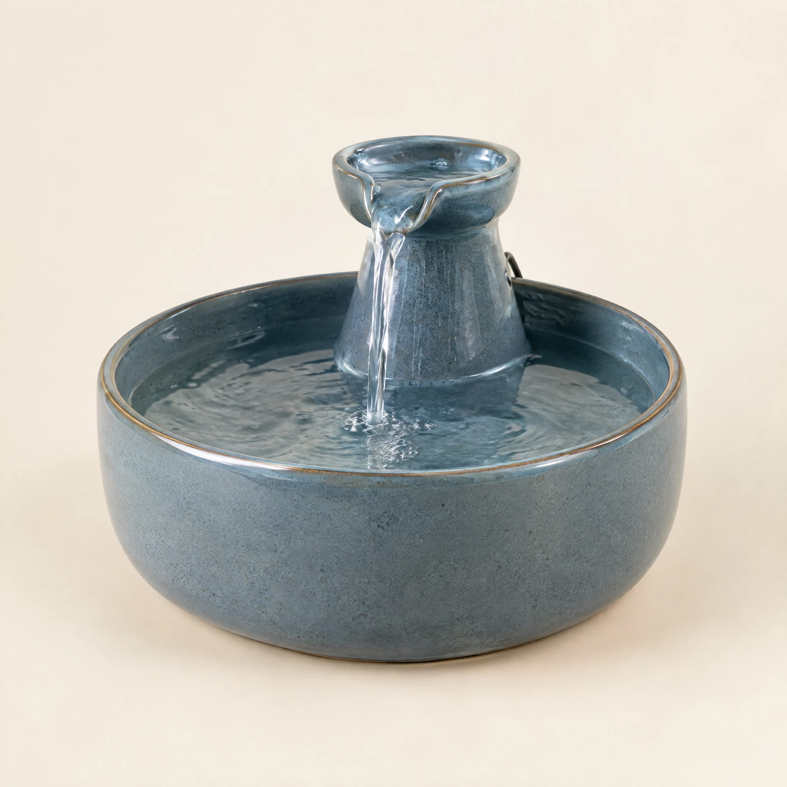 A blue-gray glazed pet water fountain with a raised spout over a wide basin, on a cream background