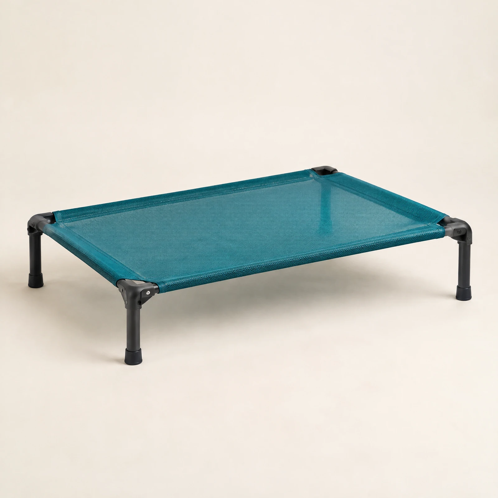 A raised dog cot with a dark gray frame and a teal open-weave sleeping surface, empty, on a cream background