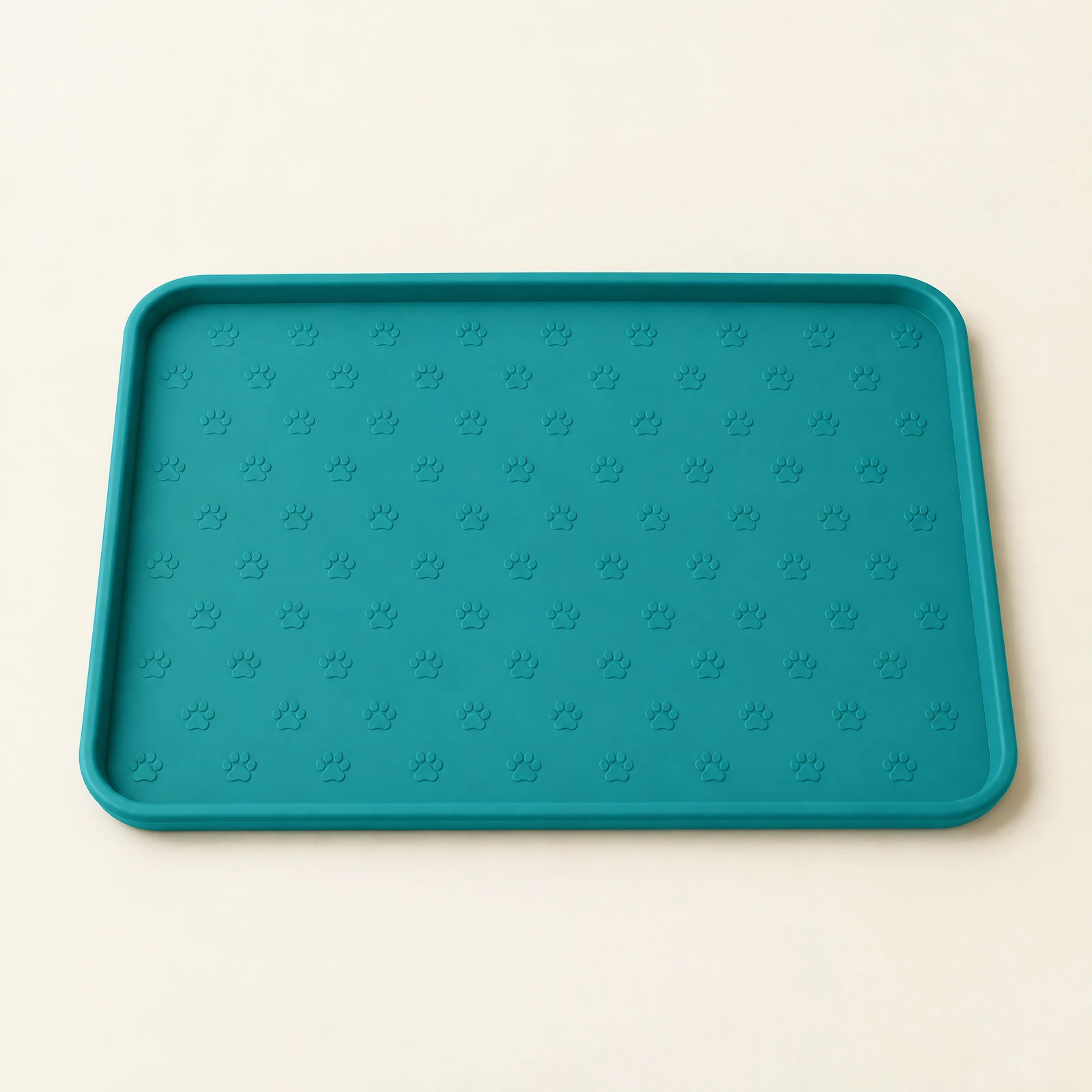 A teal rectangular pet bowl mat with a raised edge and a paw-print pattern, photographed from above on a cream background